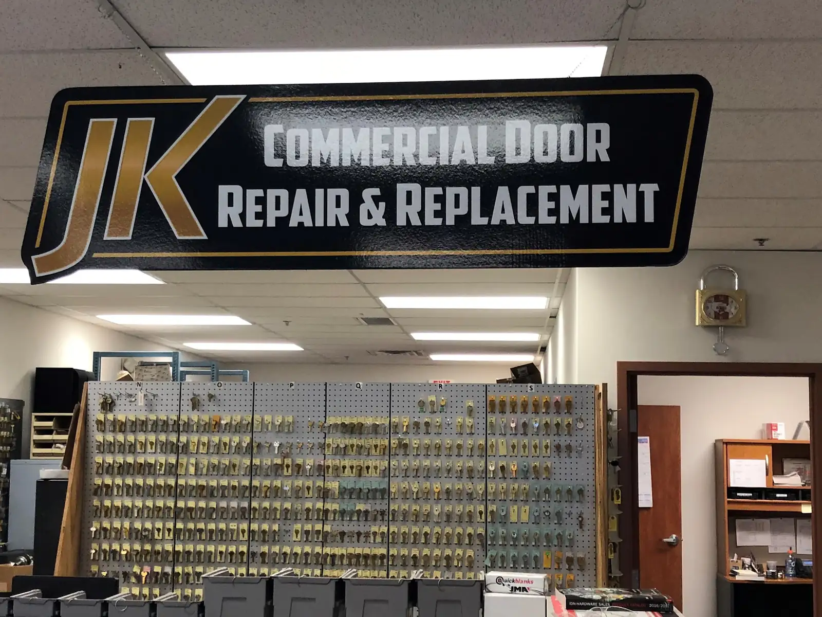 The JK Commercial Door Repair & Replacement sign hanging over the key display inside the shop